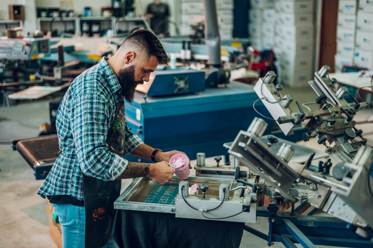 male-worker-pressing-ink-on-frame-while-using-the-printing-machine-in-a-workshop.jpg